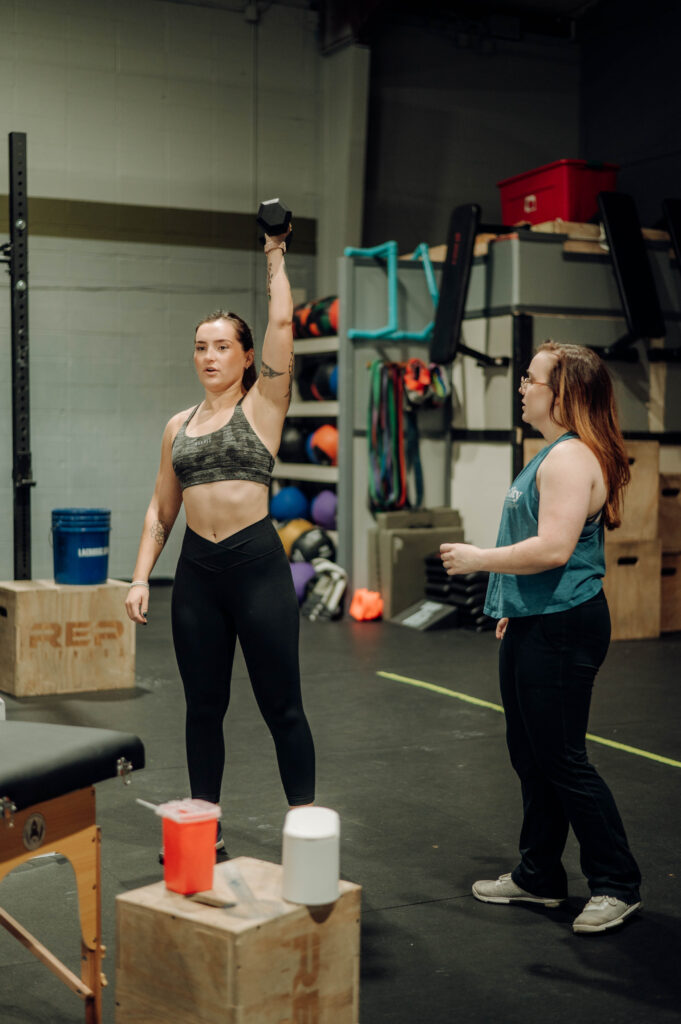 Crossfitter performing overhead press while being coached on form
